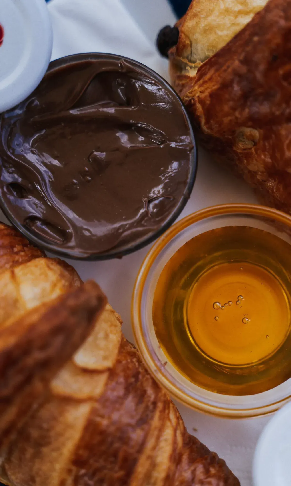 Frische Croissants von oben fotografiert, dazu Schälchen mit Schokoladencreme und goldenem Honig.
