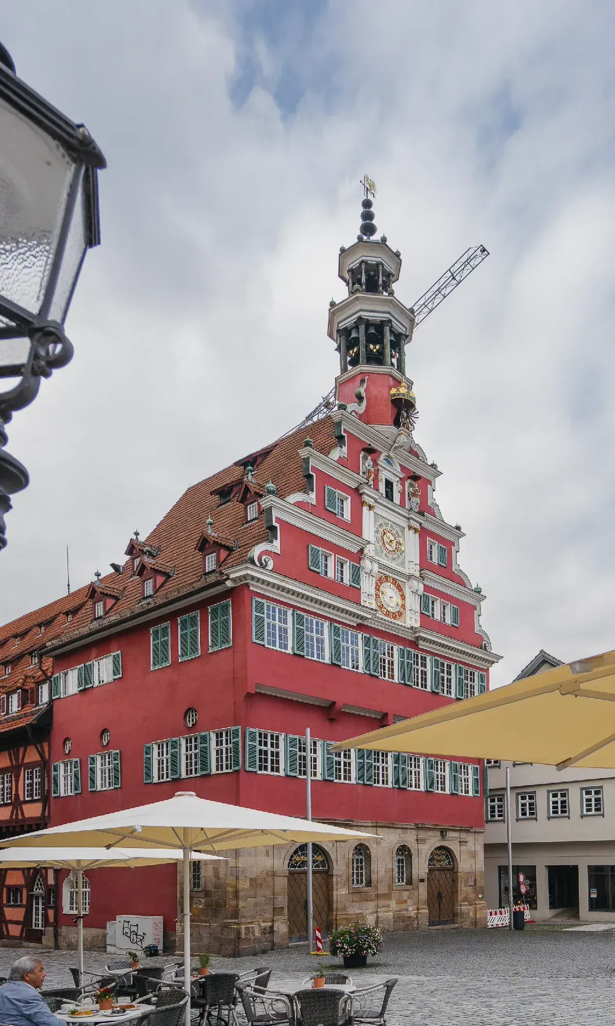 Das rote Alte Rathaus von Esslingen mit astronomischer Uhr, davor die Sonnenschirme und Tische der Cafés auf dem Rathausplatz.