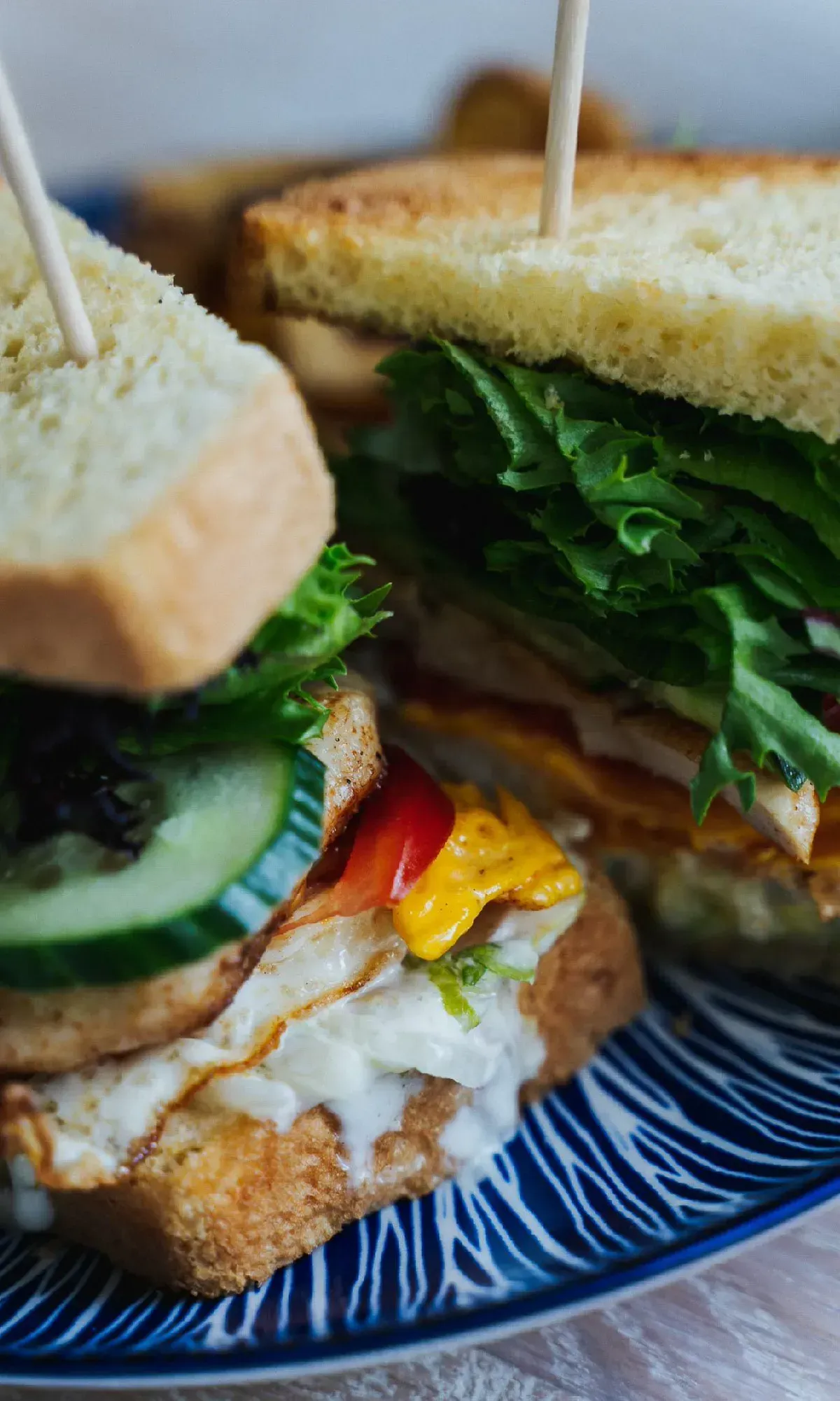 Aufgeschnittenes Sandwich mit knusprigem Toast, Salat, Gurke, Ei und Tomate auf blau gemustertem Teller.