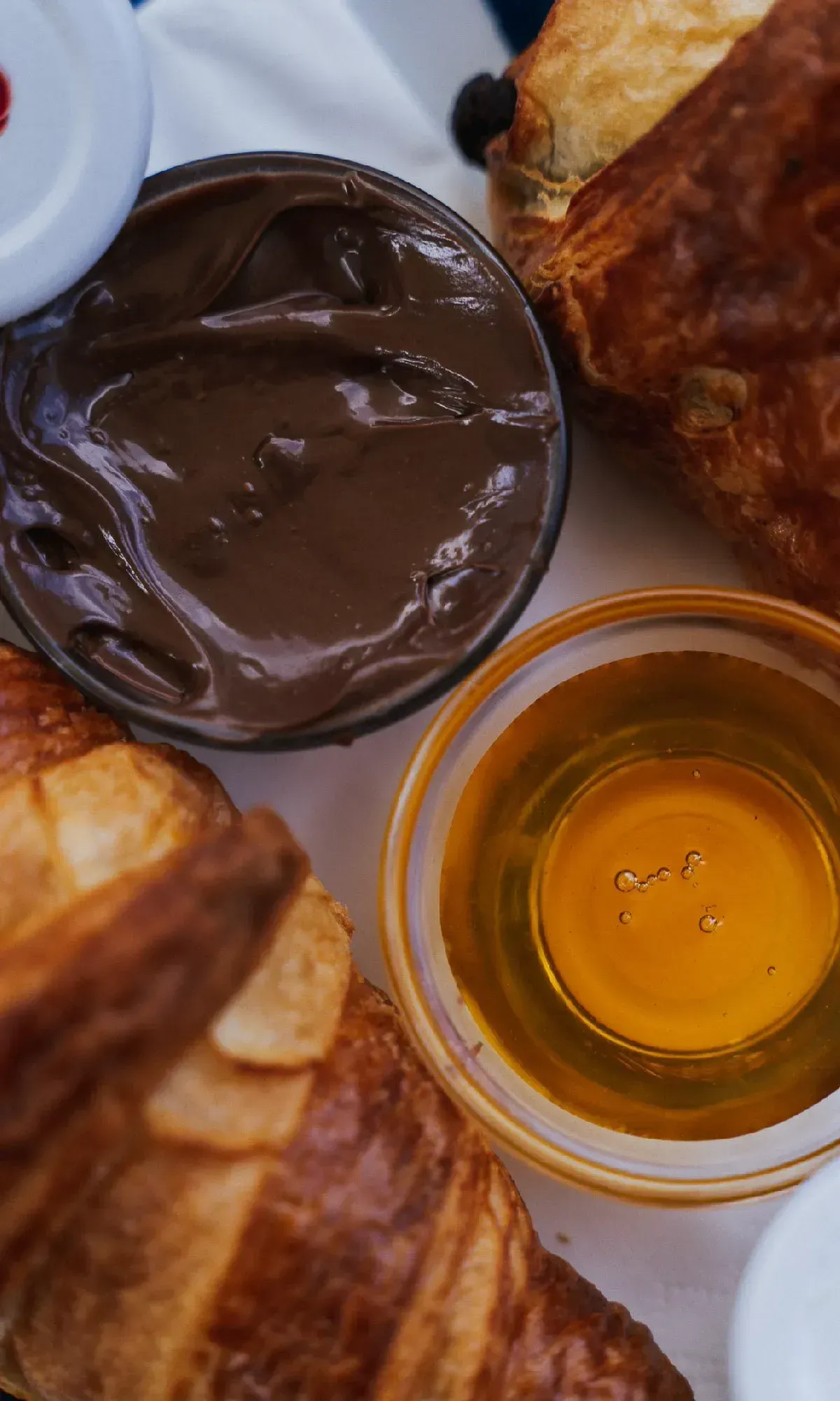 Frische Croissants von oben fotografiert, dazu Schälchen mit Schokoladencreme und goldenem Honig.
